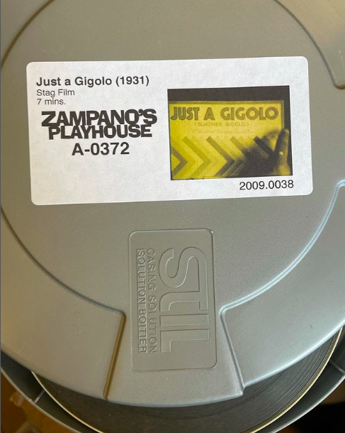 Stag Film with sticker on top with the label Just a Gigolo (1931) and Zampano's Playhouse with the number A-0372. Next to the label is an image of Just A Gigolo in a print