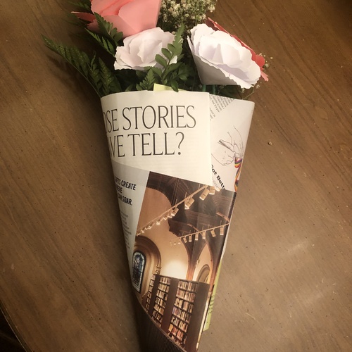 A bouquet of paper flowers wrapped in paper that reads "What Stories Can We Tell?"